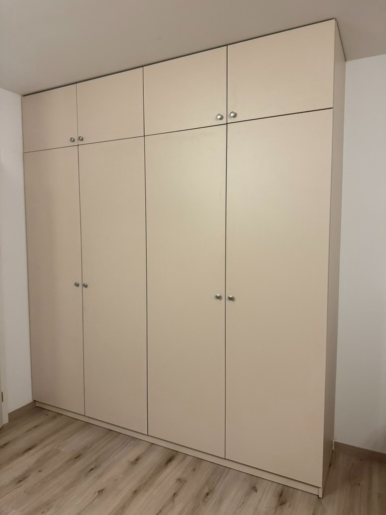Realizace šatní skříně na míru s nástavcem ke stropu Meublex – otevírací dvířka v krémovém matném dekoru a kovové knopky
